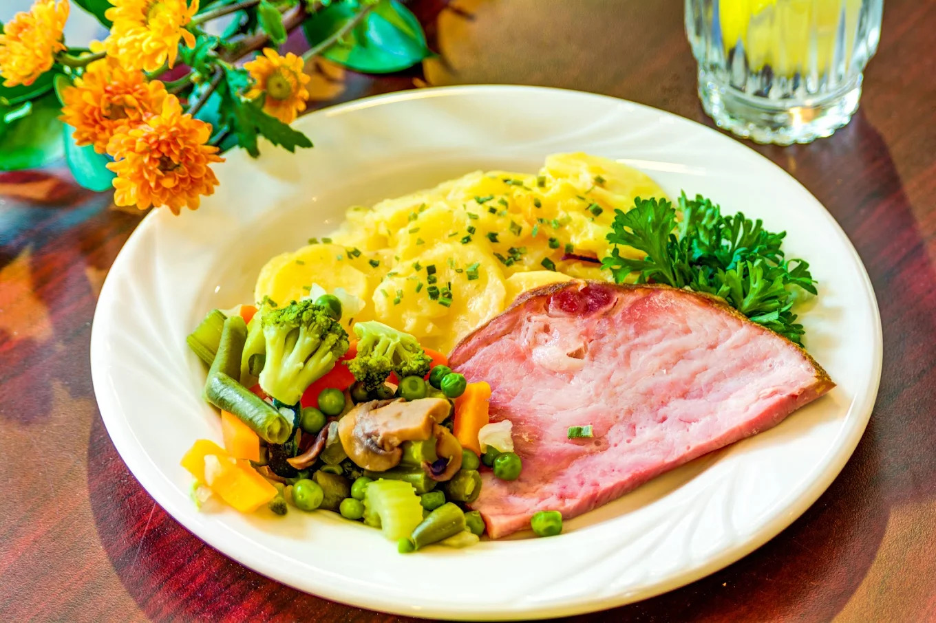 A plated meal of sliced ham, scalloped potatoes and mixed vegetables