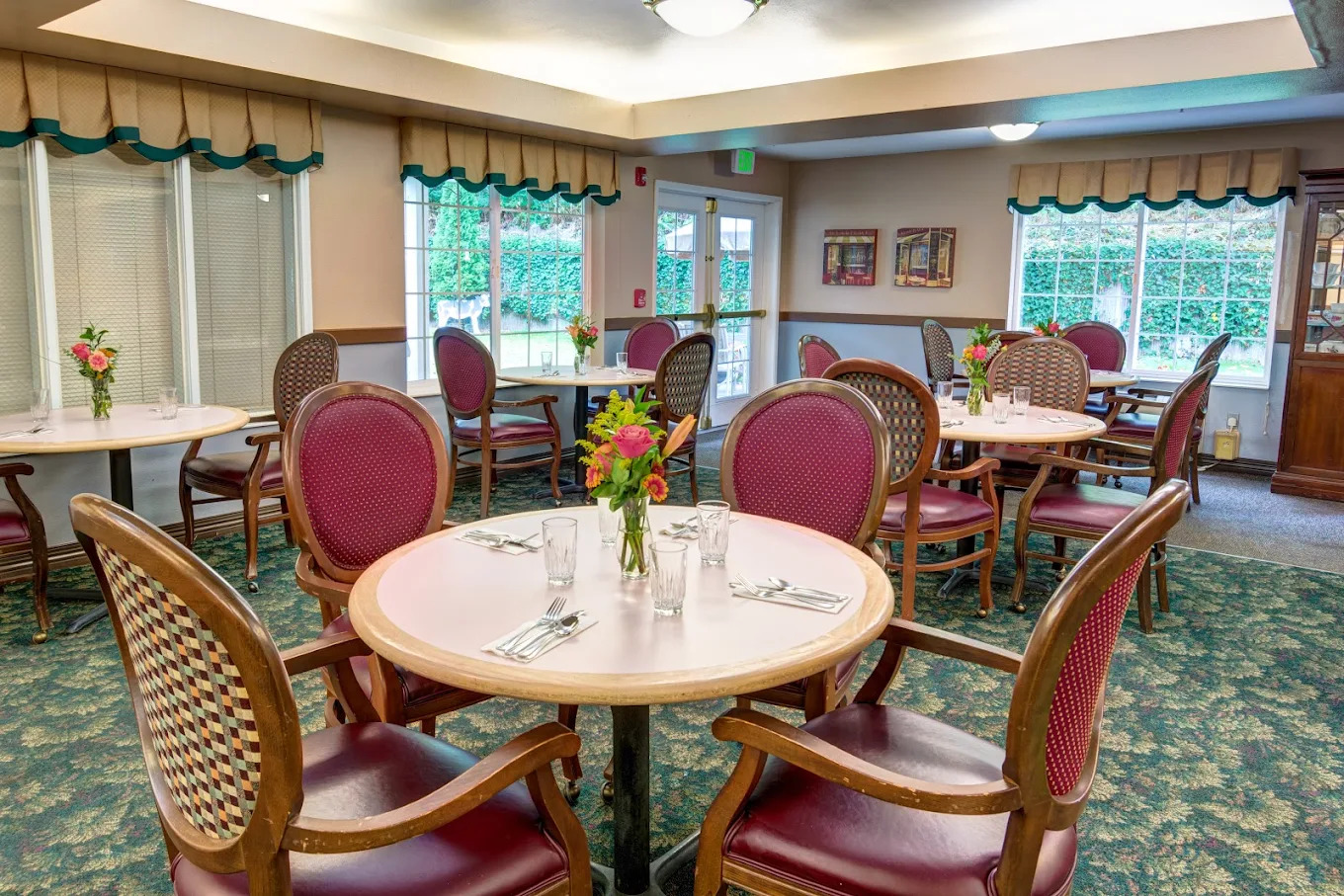 Main dining room with round cream tables, burgundy chairs and fresh flowers on each table