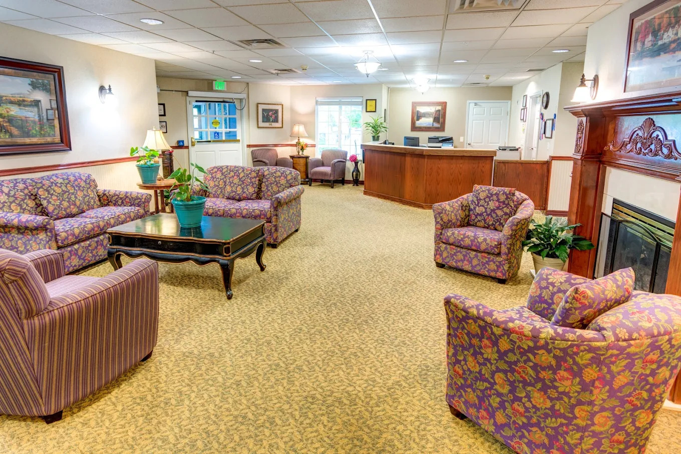 Main lobby with a reception desk, purple floral sofas, striped armchairs and a fireplace