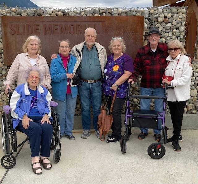 Residents of Cascade Valley Senior Living on an outing to the Oso Slide Memorial, standing together with wheelchairs and walkers in front of the stone memorial wall